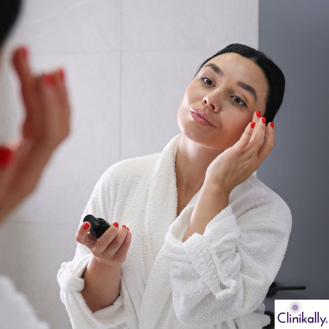 Woman applying OTZ 10 skincare serum while looking in bathroom mirror
